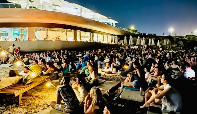 PEOPLE AT THE BEACH LOOKING AT A SCREEN